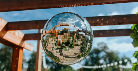 A disco ball hangs outside below a pergola, with a band of lights in the background