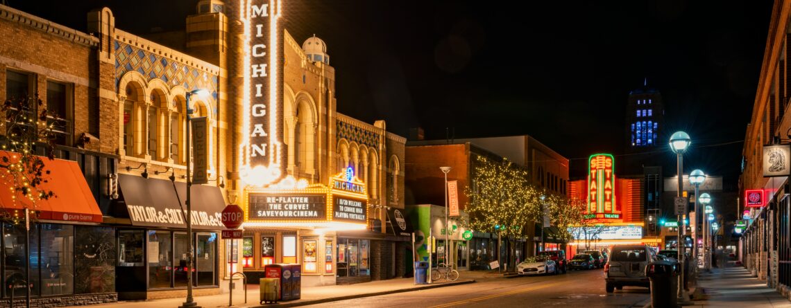 The Michigan Theater and State Theater in Ann Arbor light up an empty roadway on a dark night with flashbulb and neon signs naming their respective storefronts.