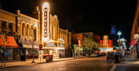 The Michigan Theater and State Theater in Ann Arbor light up an empty roadway on a dark night with flashbulb and neon signs naming their respective storefronts.
