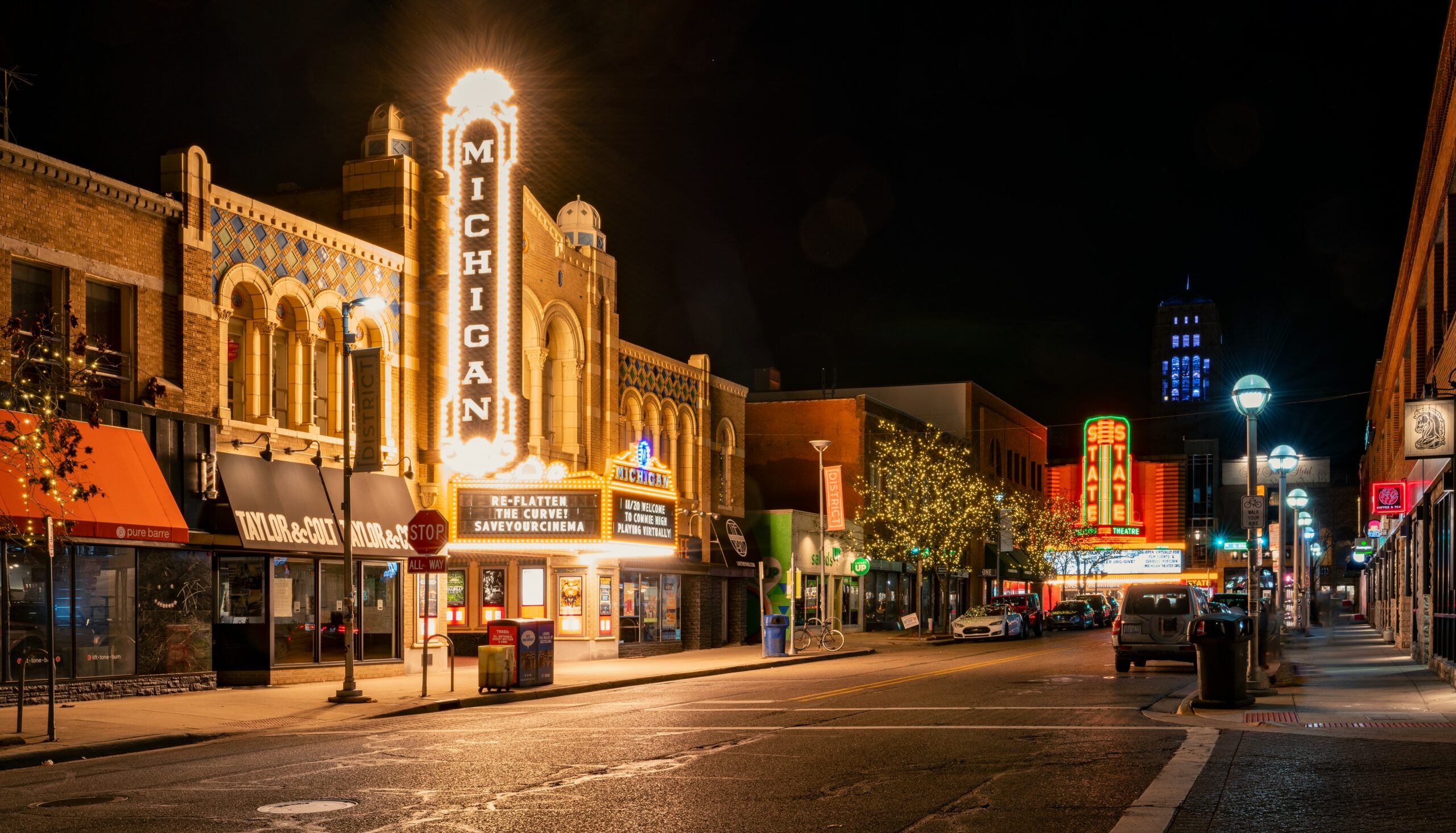 The Michigan Theater and State Theater in Ann Arbor light up an empty roadway on a dark night with flashbulb and neon signs naming their respective storefronts.