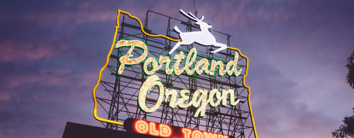 An Oregon-shaped neon sign reading 'Portland Oregon Old Town' and featuring a leaping stag perches atop a building. The sky is purple at sunset.