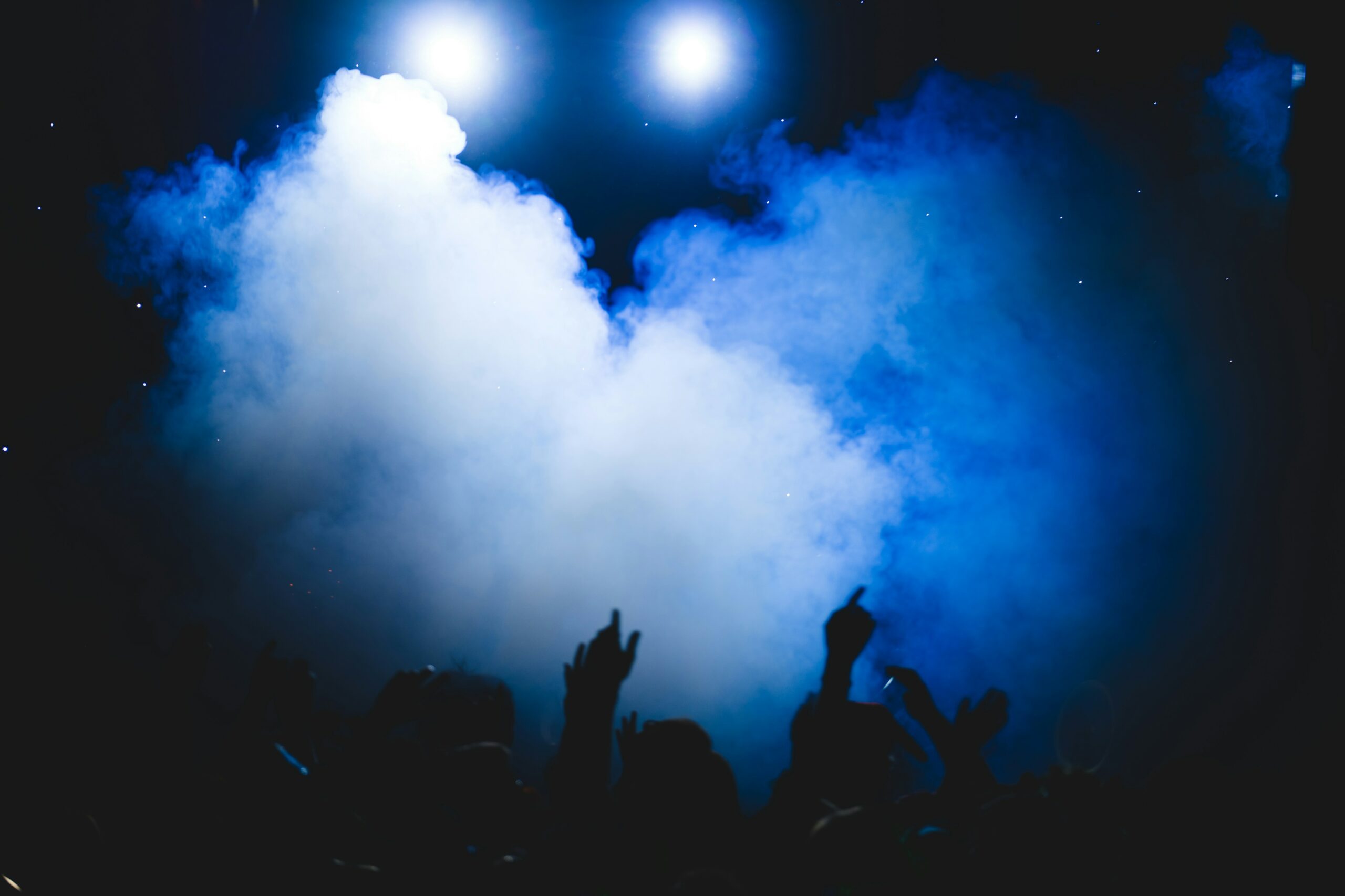 The silhouette of people raising their arms and partying at the base of a blue cloud of smoke at a stoner event.
