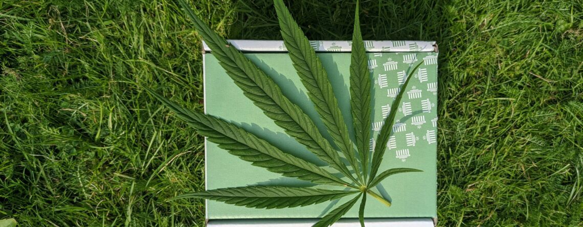 A cannabis leaf lays atop a weed wedding favor on a grassy lawn.
