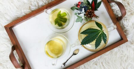 Cannabis leaves, tea and a small arrangement of weed wedding flowers are atop a tray sitting on a fuzzy white surface.