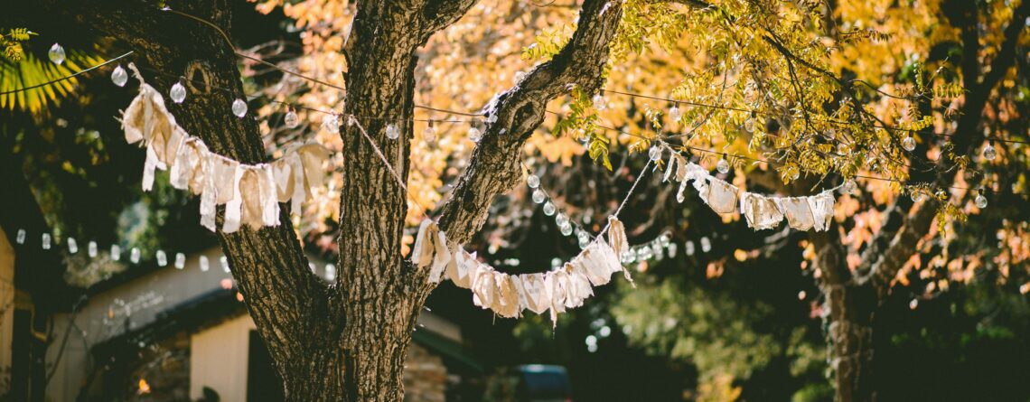 A tree with colorful bunting is over tables set with white cloths and tableware for a wedding.