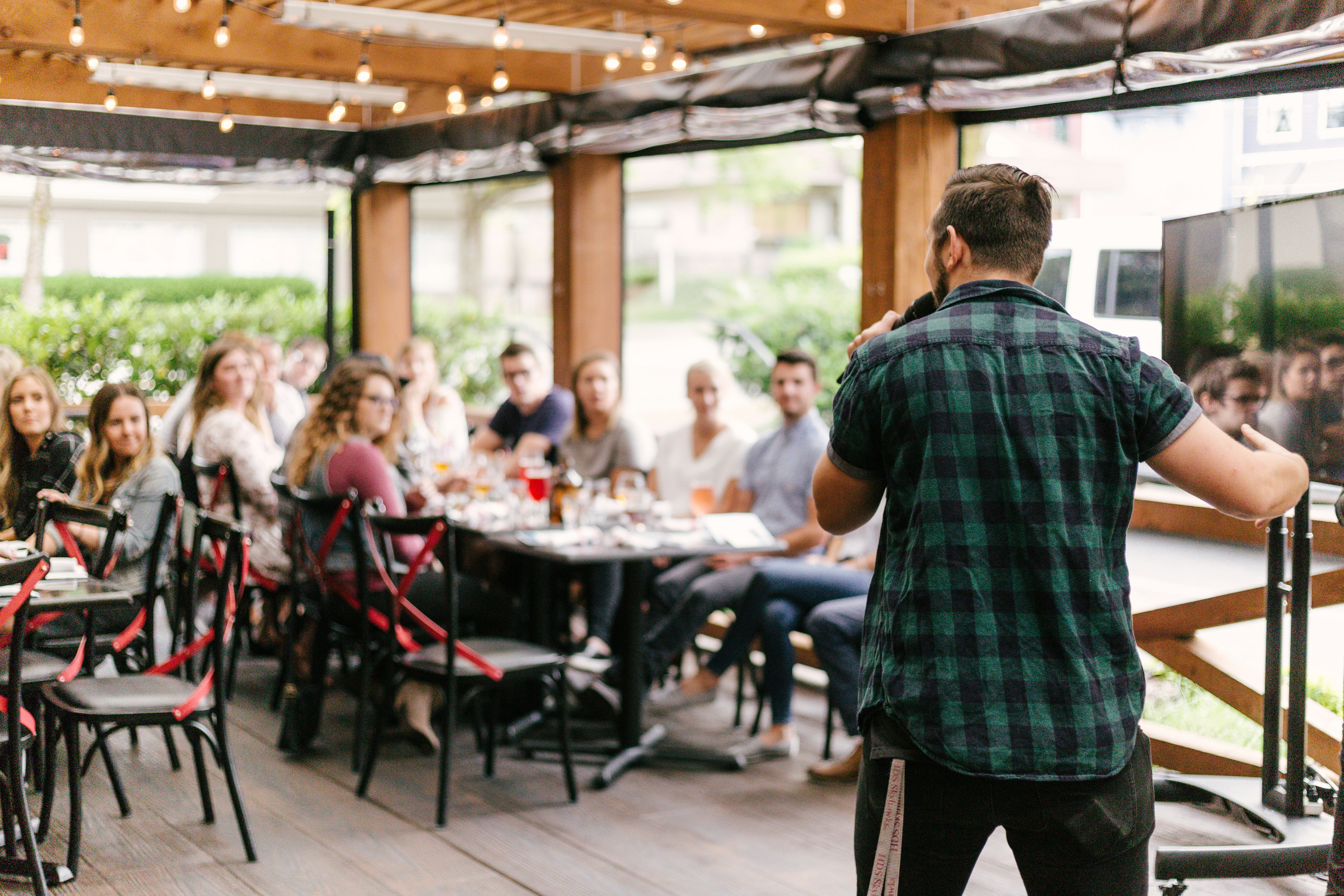 A man stands in front of a small crowd of employees at a work event, holding a microphone and speaking as they listen and watch.